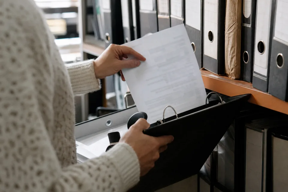 Księgowa wpina wydrukowane potwierdzenie do segregatora archiwum
